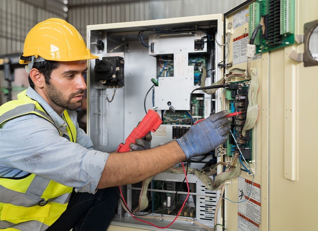 Insurance Solutions - Male Electrician Repairing and Maintaining a Operational Electric System in a Factory